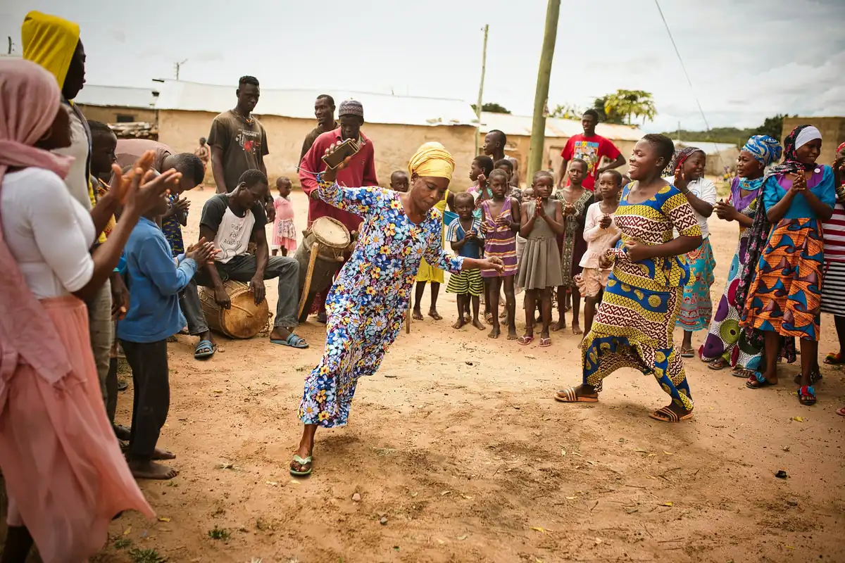 Drumming and dancing in a village compound, with neighbours gathered round watching