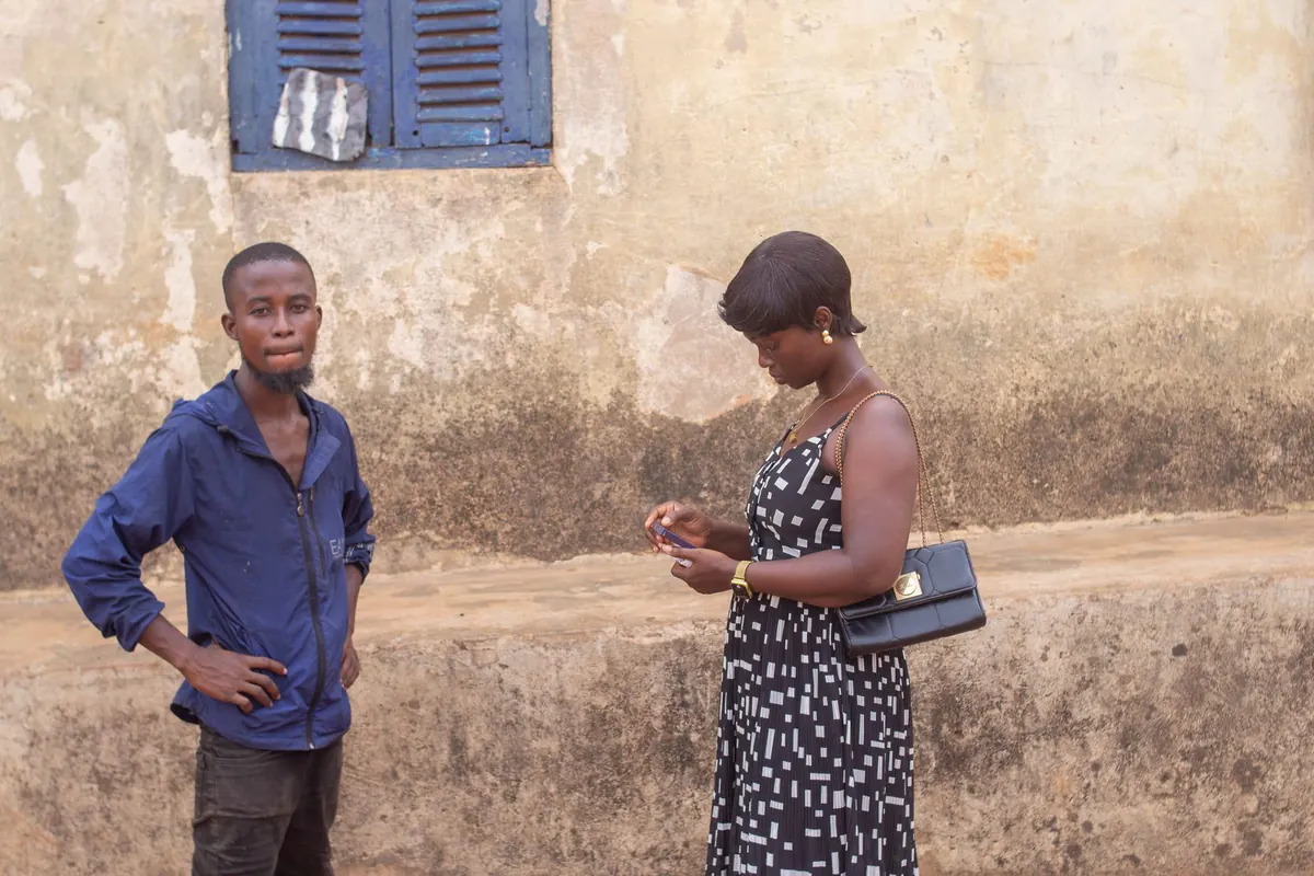 Two young people outside a weathered building on a street in a Ghanaian town