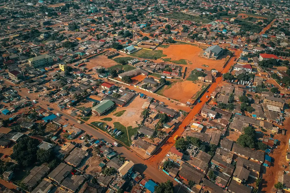A dense Ghanaian town seen from the air, laterite roads running between tin-roofed compounds