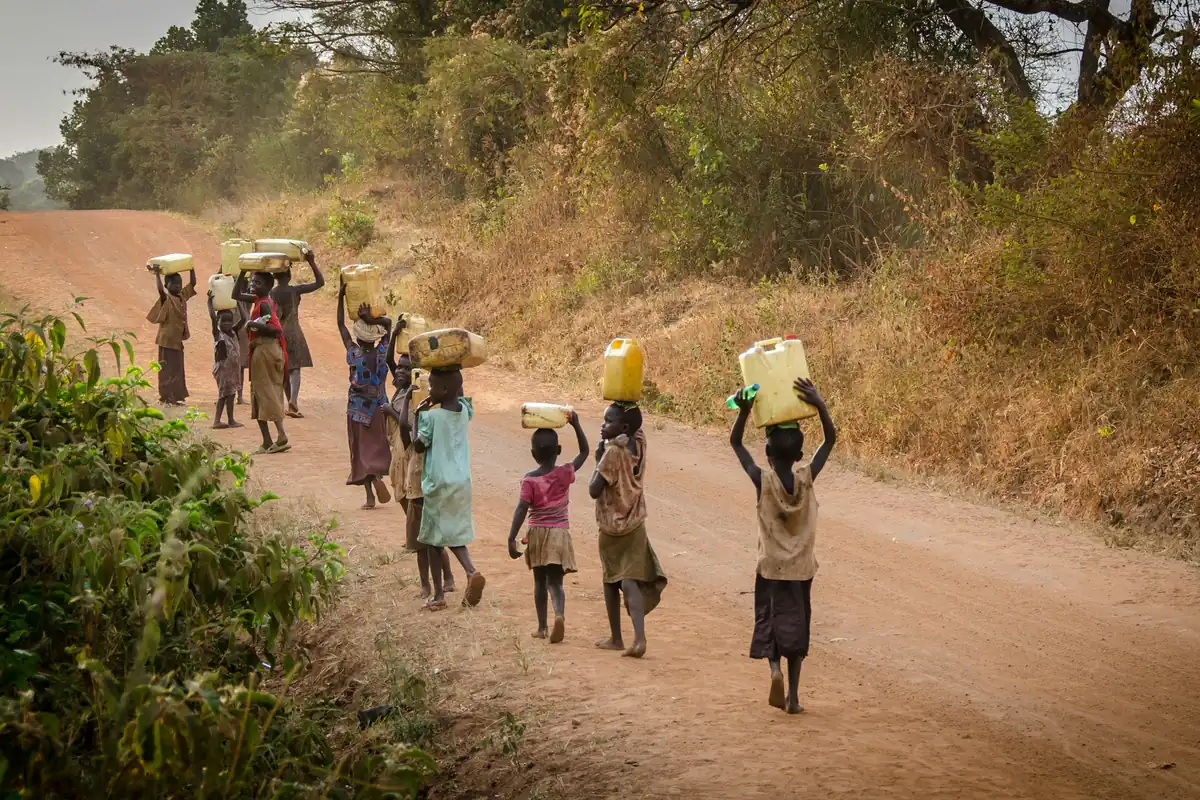 People walking a dirt road carrying water containers on their heads
